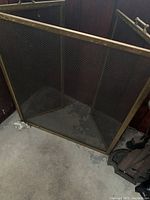 Metal fireplace screen with three hinged mesh panels and bronze-colored frame