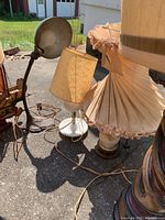 Five assorted vintage lamps with varying bases and shades shown outdoors.