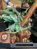 Box with artificial fern in brown square pot with cream decorations, partial view of wooden artwork with fringe and colorful circles