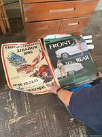 Three rolled posters partially unrolled on a floor showing the Warbird Gathering Airshow and Sherman car ads