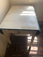 Photo of vintage rectangular enamel table with metal legs and a drawer underneath, showing visible wear, discoloration, and chipping paint.