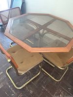 View of octagonal glass top table with wooden frame and three brown cushioned chairs with brass metal frames and cane backs beneath it
