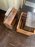 Photo showing two wooden crates with distinct markings and a vintage washboard leaning against a wall on a worn wooden floor.