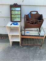 Photo shows a white 3-tier shelf unit, a mirror with wooden brown frame, a wooden magazine holder, and a glass-top wooden cart with wine bottle racks and metal frame on wheels.