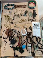 Overview of entire lot showing multiple necklaces, bracelets, rings, earrings, pendants, stones, cufflinks, tie bars, and 10k necklace labeled on paper