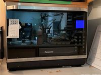Front view of Panasonic convection oven with control panel and blue display screen visible. Oven is on a countertop with reflection in glass door.