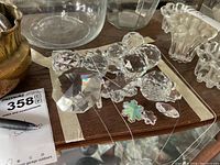 Clear multifaceted crystal pieces of assorted shapes including octagon, spheres, hearts, flower and teardrops arranged on a wooden surface and glass tray