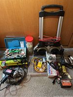 Photo showing the front view of the entire lot including dolly, power tools, sewing kit, zip ties, cords, and hardware items on carpet in front of wooden wall