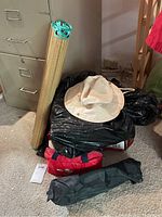 Lot items grouped including rolled beach mat, beige bucket hat, red first aid kit bag, folded umbrella, and cane near filing cabinet.