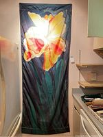 Floral flag with large yellow and orange flower on dark green background hanging vertically.