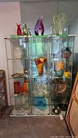 Three tall glass shelving units filled with glassware and decorative items, showing full front view for visual condition and structure.