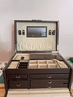 Closed up view of the jewelry box interior showing the compartments, ring rolls, elastic pouch, and mirror on lid's underside.