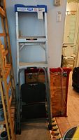 Full view of 5-foot Lite ladder, black Rubbermaid step stool folded, and wooden dolly with red rope in background