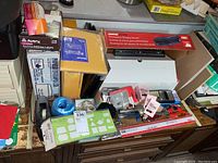 Photo showing assorted office supplies including boxed GBC Presentation Binding System, Avery labels, envelopes, tape dispenser, blue string spool, and assorted small items on a desk.