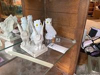 Set of owl figurines on glass shelf, including two white owls with yellow eyes, two marble-style owls with raised wings on base, and two small glass owls.