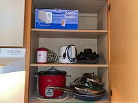 Image showing a cabinet with a boxed 2-slice Toastermaster toaster, white electric kettle, and several frying pans along with a Rival rice cooker.