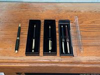 Lot of five pens, four displayed in cases, one pen outside a case on a wooden surface