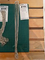 Six chains on green cutting mat with lot tag reading “6 Sterling Chains 25"”