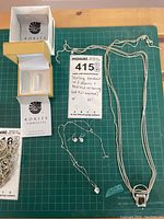Photo showing multiple sterling silver chains, including a 25 inch chain, with a ring pendant on one chain, and Korite Ammolite branded boxes for necklace and earrings.
