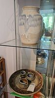 Stoneware vase and decorative plate with stoneware creamer, sugar bowl, and toothpick holder displayed on glass shelf