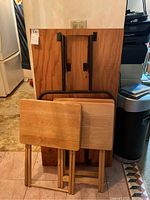 Folded condition of the four tables seen leaning against wall, showing tabletops and folded legs.