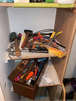 Photo showing a wooden shelf with an assortment of hand tools including hammer, pliers, clamps, black mallet, and a boxed screwdriver set inside a wooden organizer