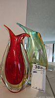 Front angled photo showing two glass vases, one red and one greenish-blue