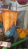 Tall vase with orange, white, blue speckled pattern next to smaller yellow vase with wavy rim