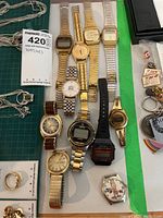 Photo showing eleven assorted wristwatches with mixed metal bands and plastic band digital watch on green background.