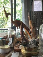 Multiple decorative items including carved wooden crane mounted on natural wood base, brass bowl with nubby edge, and silver plated coaster on ceramic base.