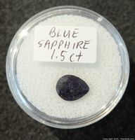 Top-down view of pear-shaped blue sapphire gemstone in container showing deep blue color and faceting.
