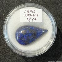 Top view of polished teardrop lapis lazuli gemstone inside a clear round display case with handwritten label 'LAPIS LAZULI 18ct'