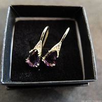 Front view of the pair of pearl-shaped amethyst and diamond earrings in a black box.