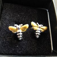 Pair of bee design stud earrings with yellow wings in a black jewelry box, showing front view.