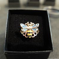 Close-up top view of silver bee ring in box showing colorful enamel wings and honeycomb pattern.