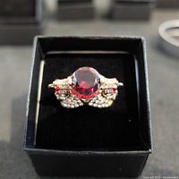 Top view of the ring showing the large round blood pigeon red ruby center stone and the detailed bird design with small clear and red stones.