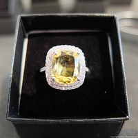 Top view of estate silver ring with cushion-cut citrine surrounded by diamond-type halo stones, set in black ring box.