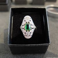 Top view of the Art Deco silver ring showing the central emerald type stone in a gold bezel with surrounding diamond type stones.
