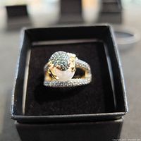 Front perspective of the silver ring showing large faux pearl with green stones and detailed pave clear stones on band.