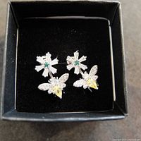 Top-down view of the bee earrings in the black box showing the emerald center, white and yellow stones making up the bee shape.
