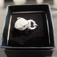 Front view of panther head silver ring with clear stones and green stones for eyes, in black jewelry box.
