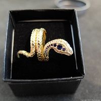 Front view of the gold-tone double strand snake ring showing the blue sapphire-type stones on the head and textured scales.