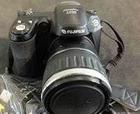 Front view of Fujifilm FinePix S5200 digital camera with attached lens and lens cap, showing branding and model number.