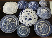 Overview of all nine plates laid out on dark surface showing various blue and white scenic and floral patterns.