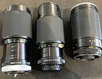 Three black camera lenses with textured rubber grips, showing aperture and focal length scales, front and mounts visible.