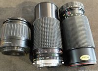 Three camera lenses displayed side by side on black surface, showing zoom and aperture markings and lens backs.