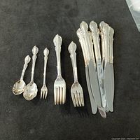 Photo showing different spoons and forks with ornate silver handles placed on a dark surface.