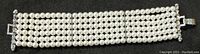 Top view of the full bracelet showing five strands of uniformly sized white pearl-type beads connected with a silver-tone clasp.
