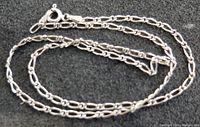 Close-up of sterling silver chain showing link design and spring ring clasp, coiled on black surface.