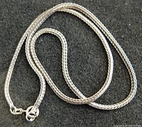 Close-up image of thick woven sterling silver chain with spring ring clasp lying on a dark background.